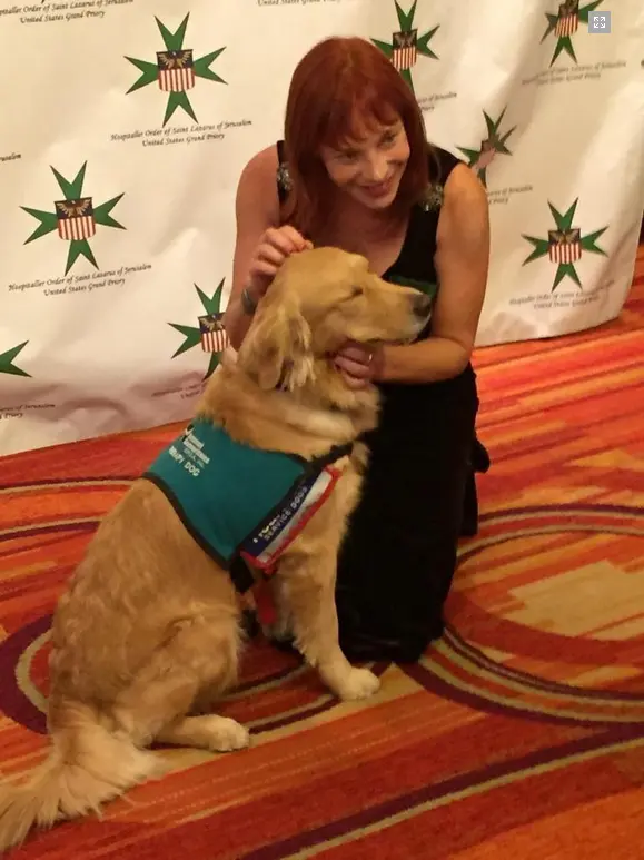 Nicole Brandon kneeling beside a golden retriever service dog at an arthritis awareness red carpet event