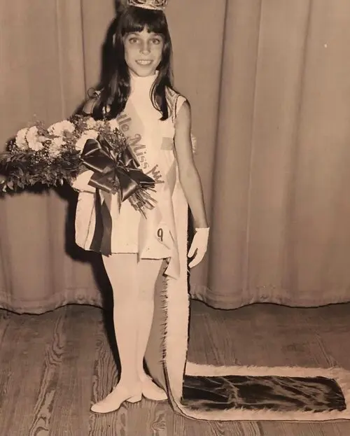 Nicole Brandon as a young girl holding flowers and wearing a crown after winning a dance award